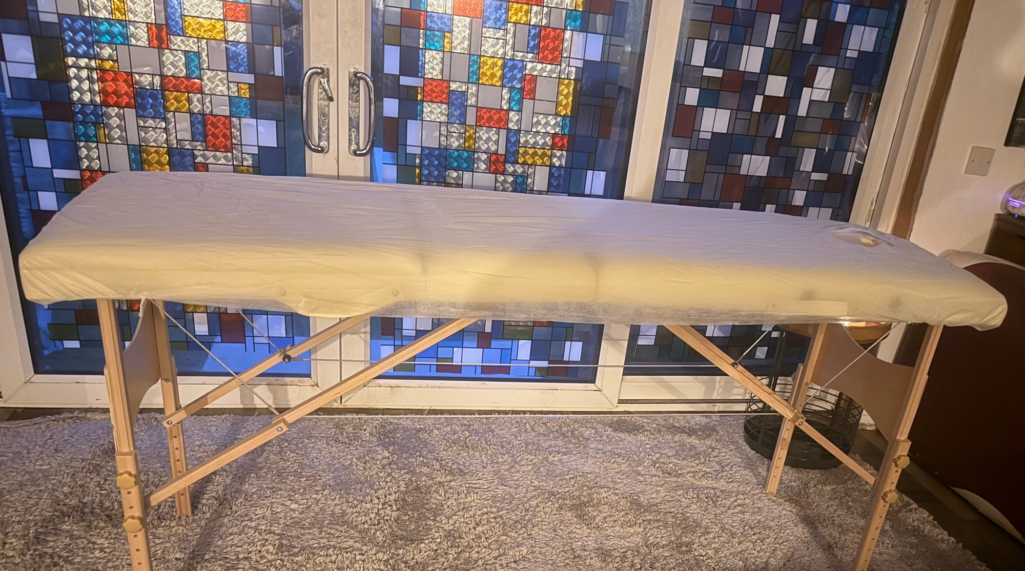 Warmly lit treatment table in front of stained-glass doors, photographed in the real home studio