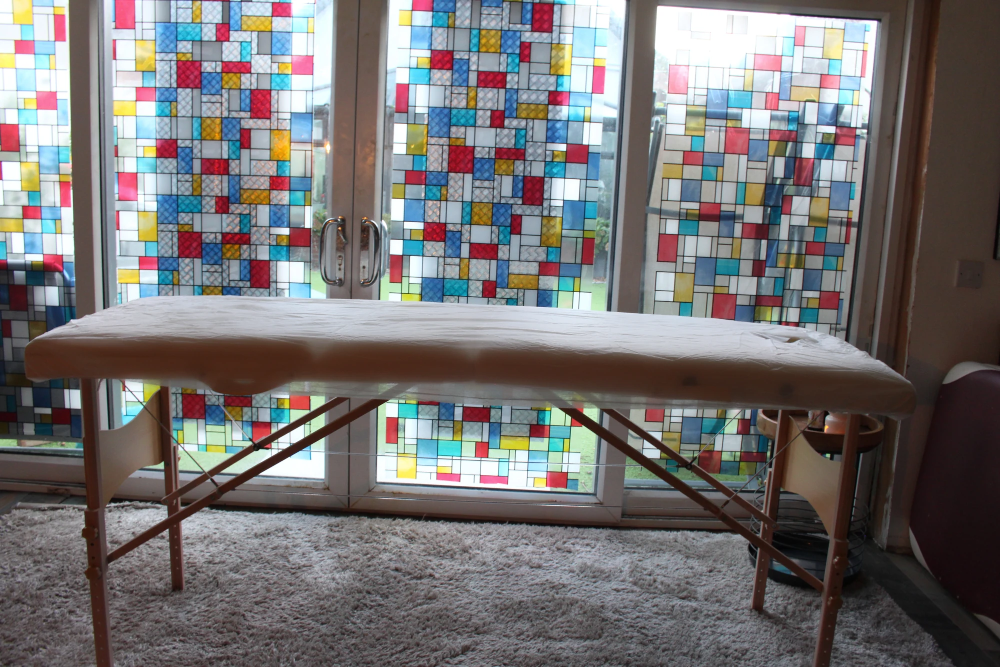 Massage table in the real Pontypridd home studio, in front of colourful stained-glass doors